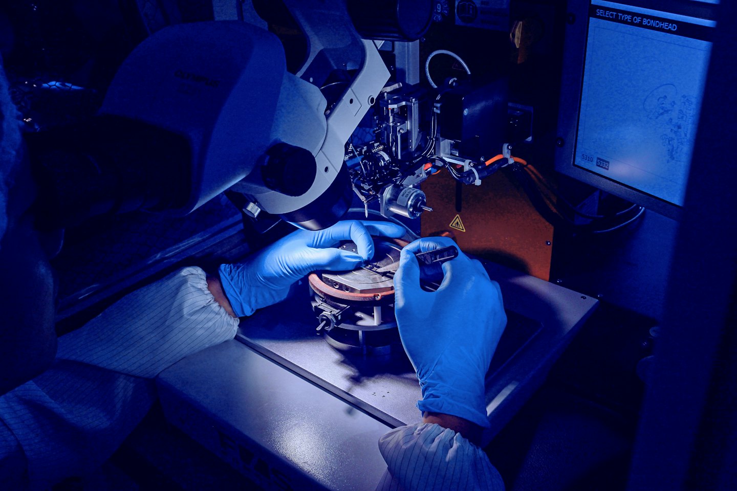 Technician in cleanroom suit works on electronic components.