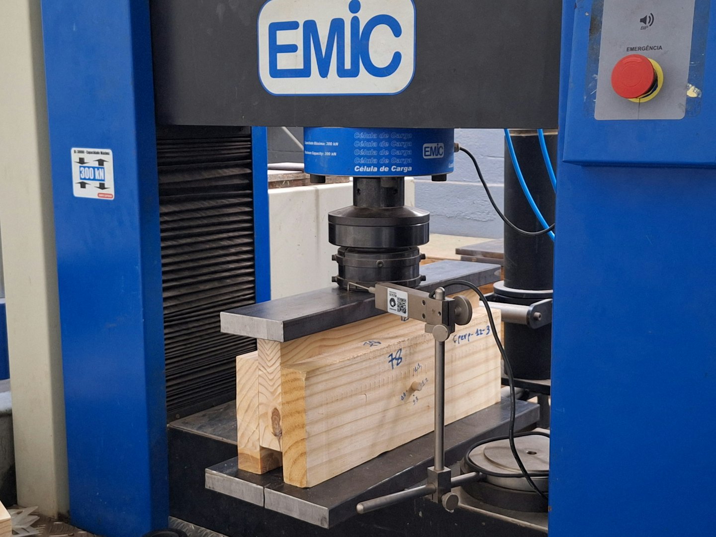 Compression testing machine pressing down on a wooden beam.